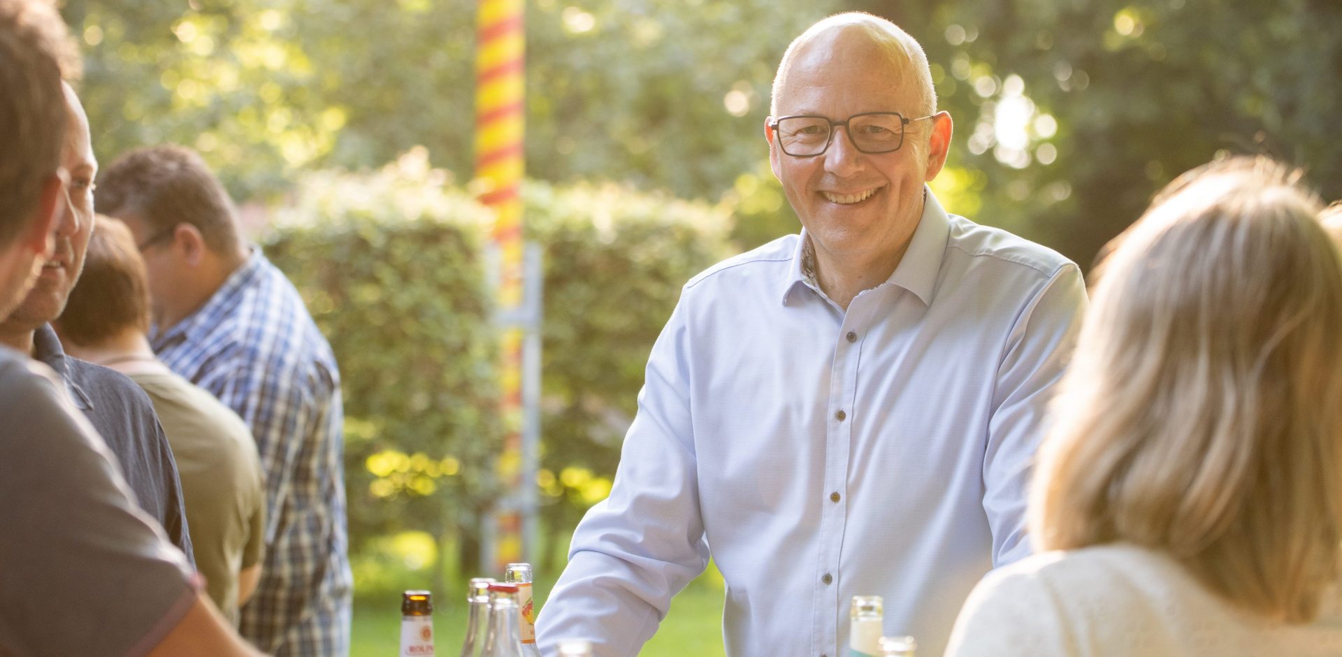 Mann, Anfang 50, steht an einem Stehtisch und hat ein Getränk in der Hand