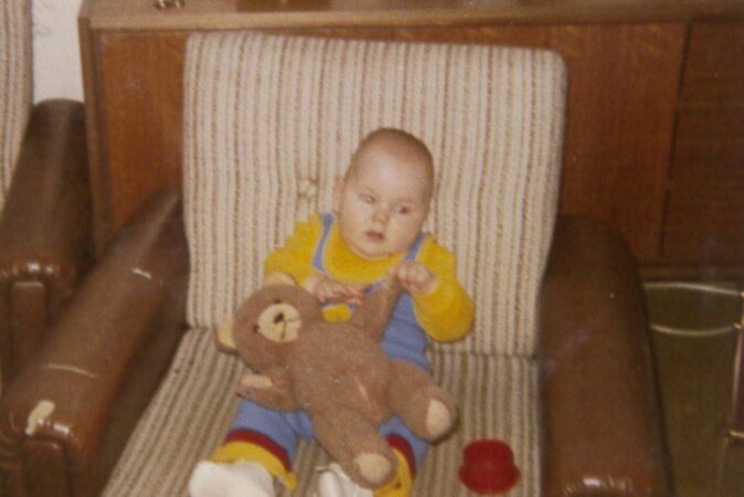 Ein fünf Monate altes Baby sitzt auf eienm Sessel und hat einen Stoffteddy in der Hand.