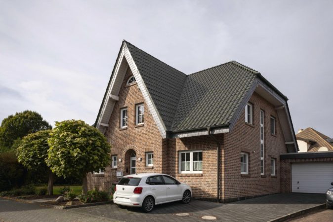 rotes Einfamilienhaus mit schwarzem Dach und weißem Auto vor dem Haus